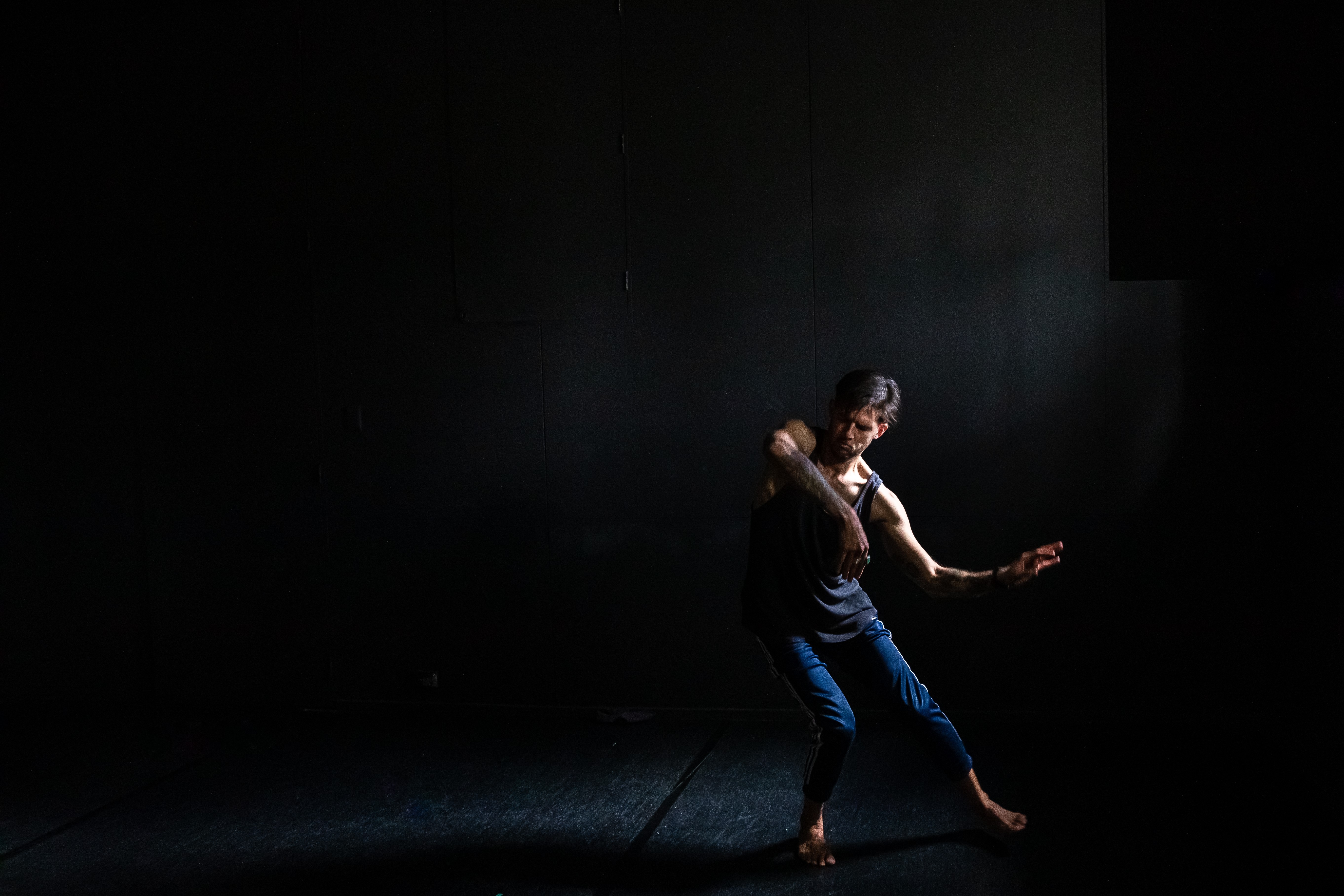 Image of a man dancing in a dark room. The features of the room are in shadow and the dancing man is illuminated. 