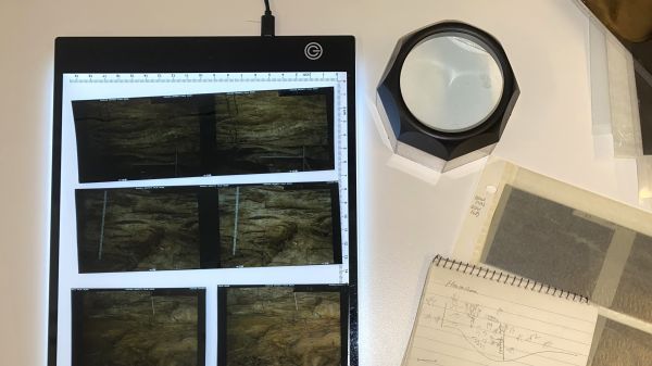 The image is of photogrammetric slides illuminated by a light box. A magnifying piece and notebook with scribbles are next to the slides.