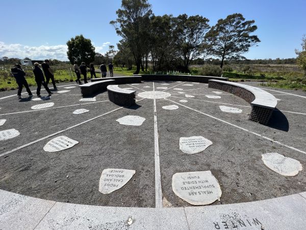 Photo of Gunditjmara seasonal calendar. The calendar is a large circle laid in stone on the ground with each season separated by a line. There are curved brick benches set in the middle of the circle.