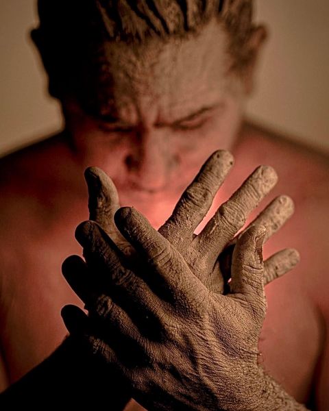 A person, with a warm light emanating from their core, warmly lighting their face, obscured by their open hands held up, palms facing in, just below their face.