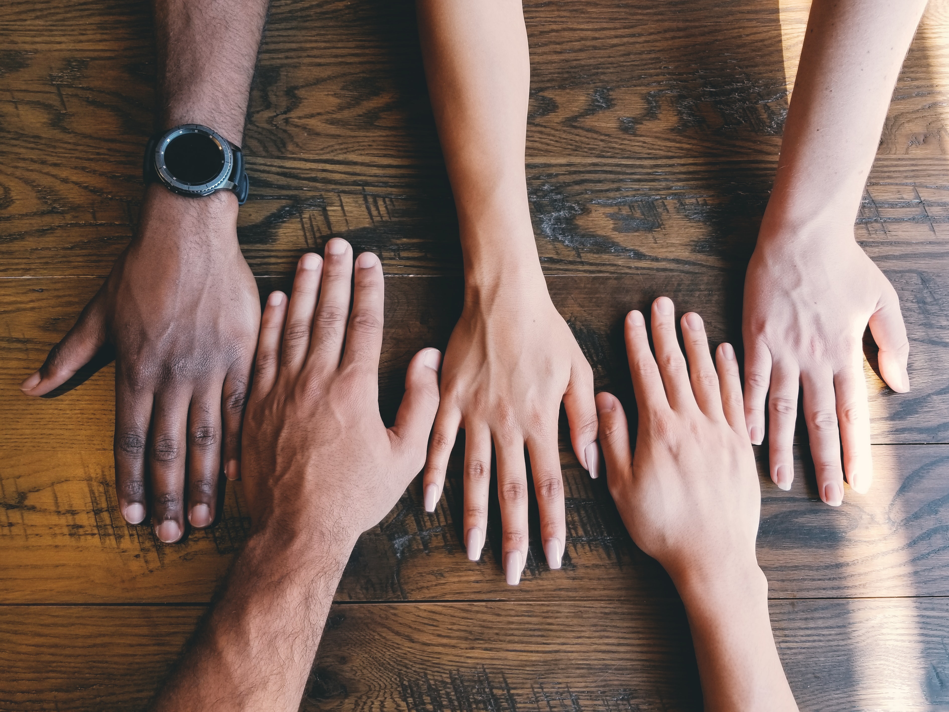 Five hands can be seen on top of a wooden surface.